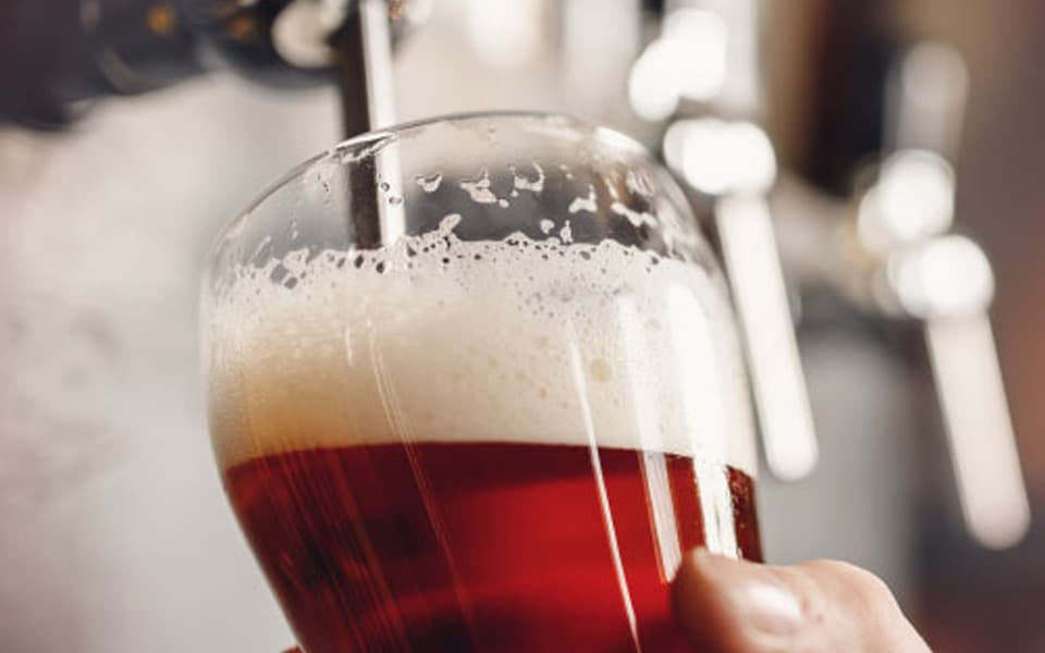 Man pouring a pint of beer from a tap into a clear glass in a bar setting