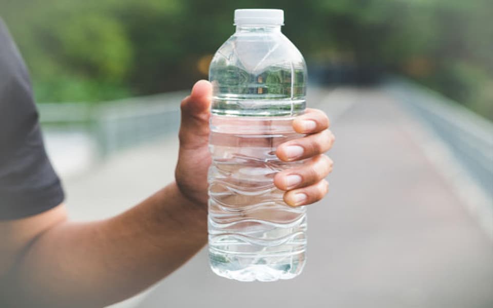Man holding a clear plastic water bottle outdoors, showcasing bottled water packaging